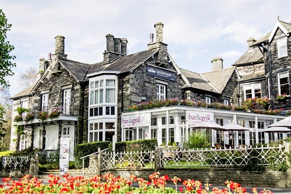 Grey stone hotel with multiple chimneys on the roof and red flowers to the front
